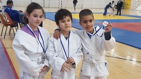 שלושה ילדים עם חליפות ג'ודו לבנות מצטלמים עם מדליה