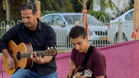 נאות הכיכר שני אנשים מנגנים בגיטרה על במה בקונטצרט